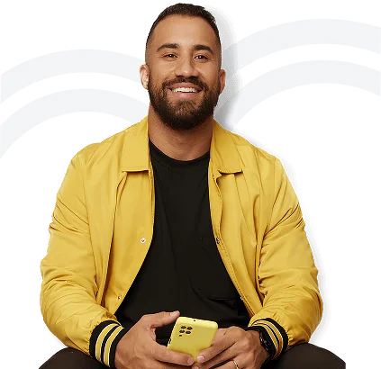 Homem sorridente com barba, roupa casual amarela e preto, sentado segurando um celular amarelo, com fundo de ondas brancas e pretas